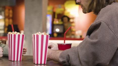 pareja feliz bebiendo y comiendo palomitas de maíz mientras hablan juntos sentados a la mesa en el snack bar del cine