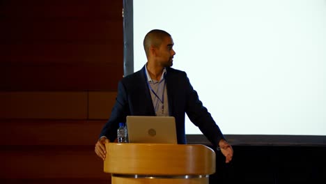 young mixed-race male speaker with laptop speaking on stage in auditorium 4k