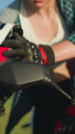 un primer plano del espejo delantero de una motocicleta roja cuando una mujer pone su casco, preparándose para un paseo