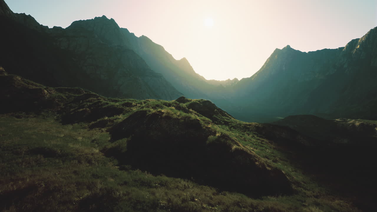 Majestic mountains under bright sun at dawn with green hills in foreground