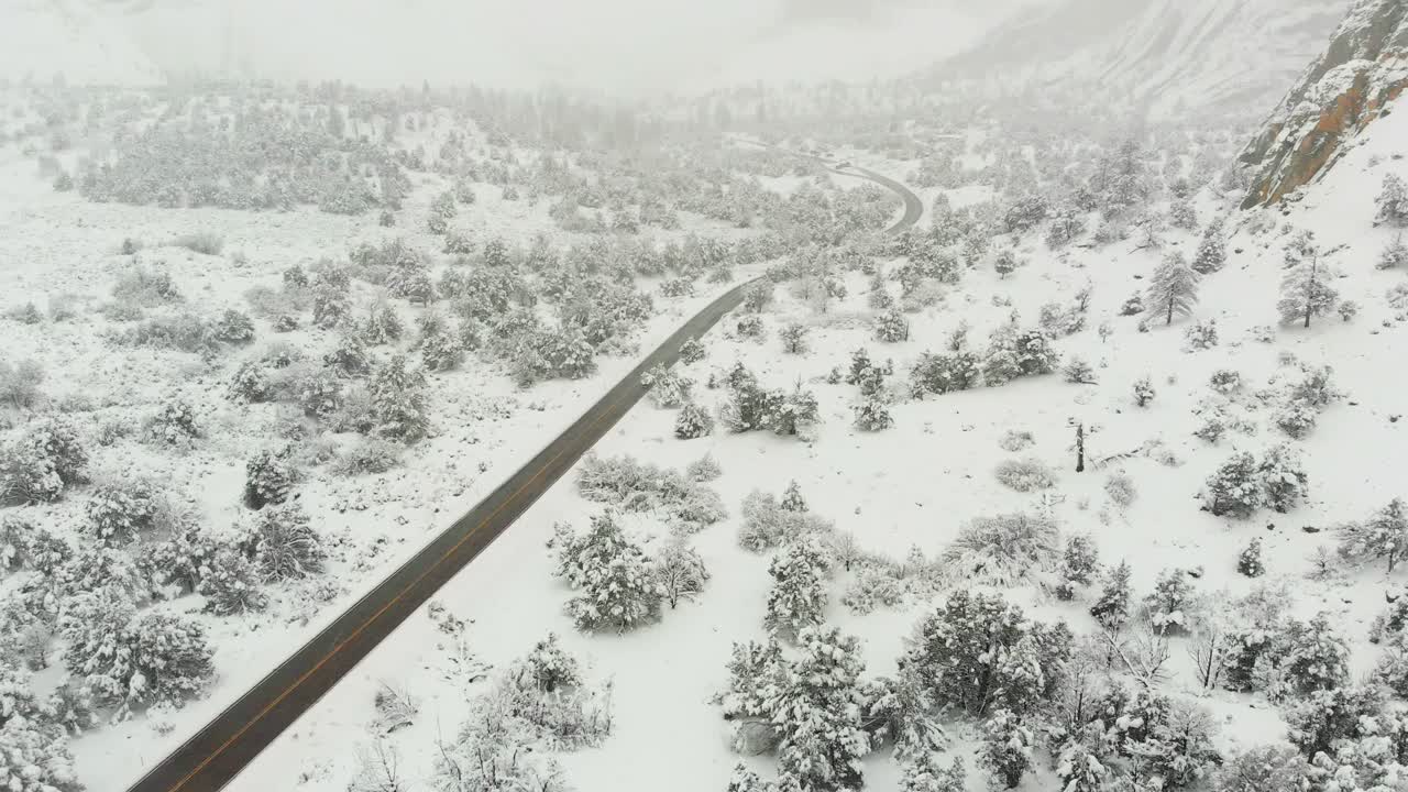 Aerial shot of a stunning snow covered landscape surrounded by mountains on a foggy day.