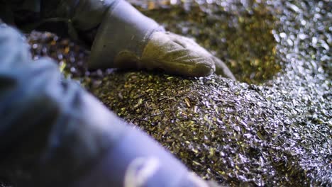 pair of gloved hands scoop up metal pieces at metal recycling plant