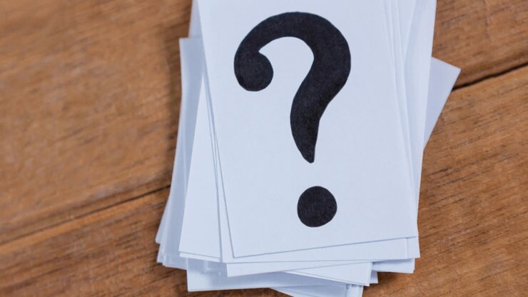 Stack of white sheets of paper with question mark signs on wooden table