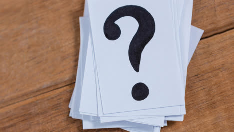 stack of white sheets of paper with question mark signs on wooden table