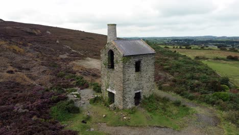 Parys-mountain-abandoned-brick-chimney-copper-mining-mill-stone-ruin-aerial-view-orbit-descending-right-push-in