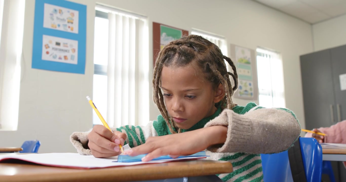 Bambino afroamericano che inizia a scrivere con una matita gialla e un righello blu in classe.