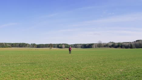 a solitary man stands in the middle of a vast green field, facing away from the camera. the open landscape and distant tree line create a sense of solitude, freedom, and contemplation.
