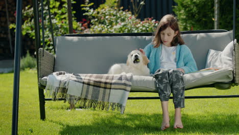 cute child plays with a golden retriever puppy. sitting in a garden swing in the backyard of a house on a clear sunny day