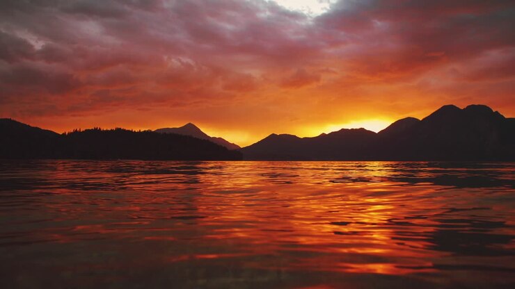 Scenic cinemagraph - seamless video loop of a beautiful and romantic sunset at mountain lake Walchensee in Southern Germany - Bavaria with moving red evening clouds and calm waves in real time