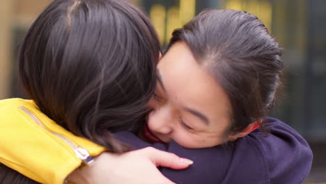 close up of two smiling young female friends meeting and hugging in urban setting together 3