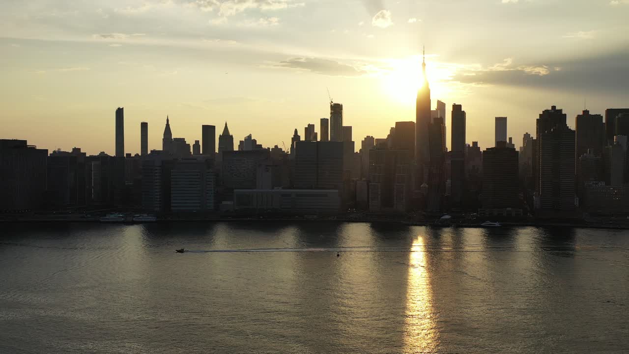 la cámara aérea de drones se desplaza a la izquierda mientras un bote flota en la misma dirección con una puesta de sol dorada - la ciudad de nueva york en el fondo