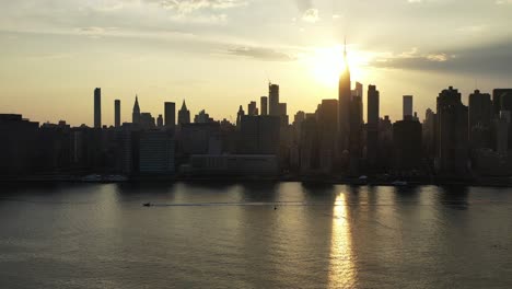 aerial drone camera pans left as a boat floats by in the same direction with a golden sunset - new york city in the background