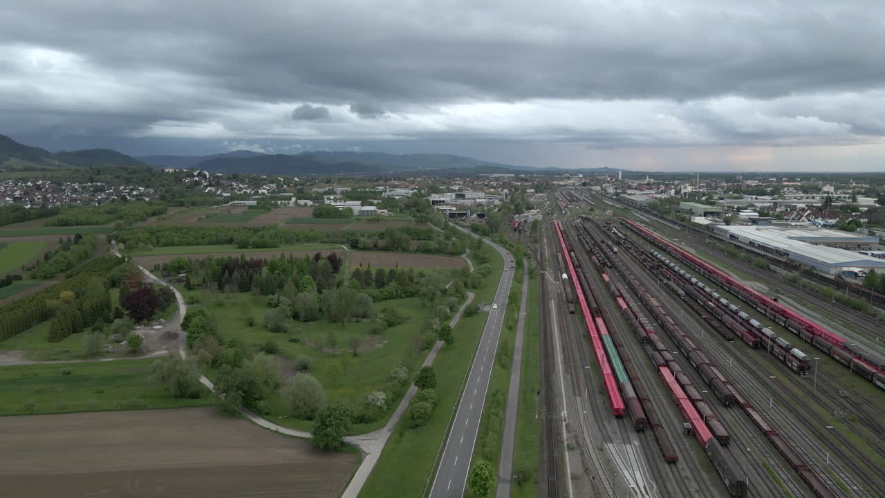 carretera con coches junto al ferrocarril con trenes, paisaje urbano en segundo plano.