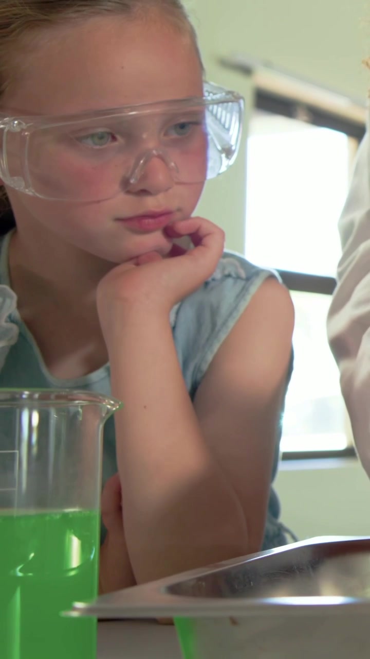 Vertical video: Curly teen using dish, causing lab coat hand, blonde observing beaker change in lab