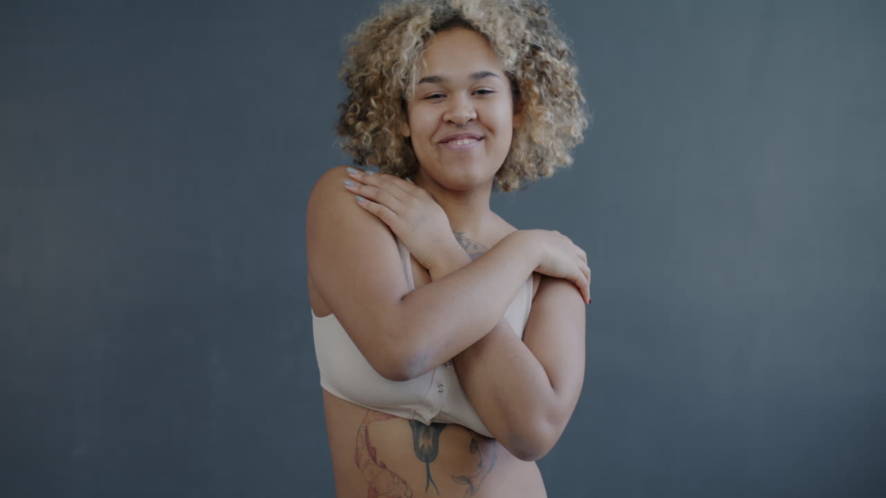 Portrait of a woman with curly hair, tattoos, and a confident smile