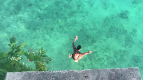 View-Of-A-Man-Jumping-From-The-Cliff-In-Salagdoong-Beach,-Siquijor-Island,-Philippines---medium-tracking-shot