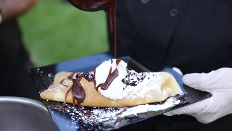 el chef rocía jarabe de chocolate con chocolate caliente sobre una deliciosa crepe