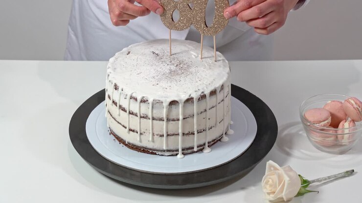 Beautiful birthday cake, decorated with macarons and a rose, being proudly presented by a female baker.
