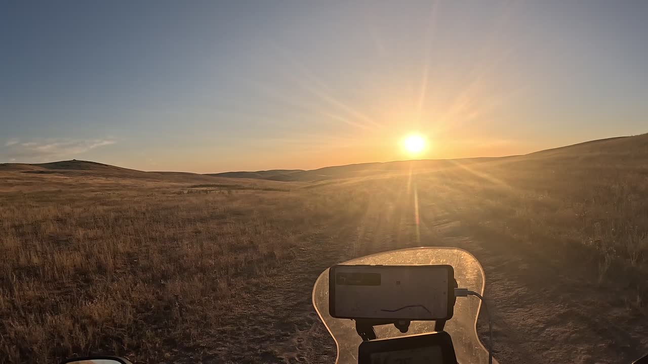 Motorcyklist kører på en grusvej gennem det bølgende bakkelandskab ved solnedgang. POV-optagelse af en eventyrcykelrejse i den fjerne vildmark under den gyldne time.