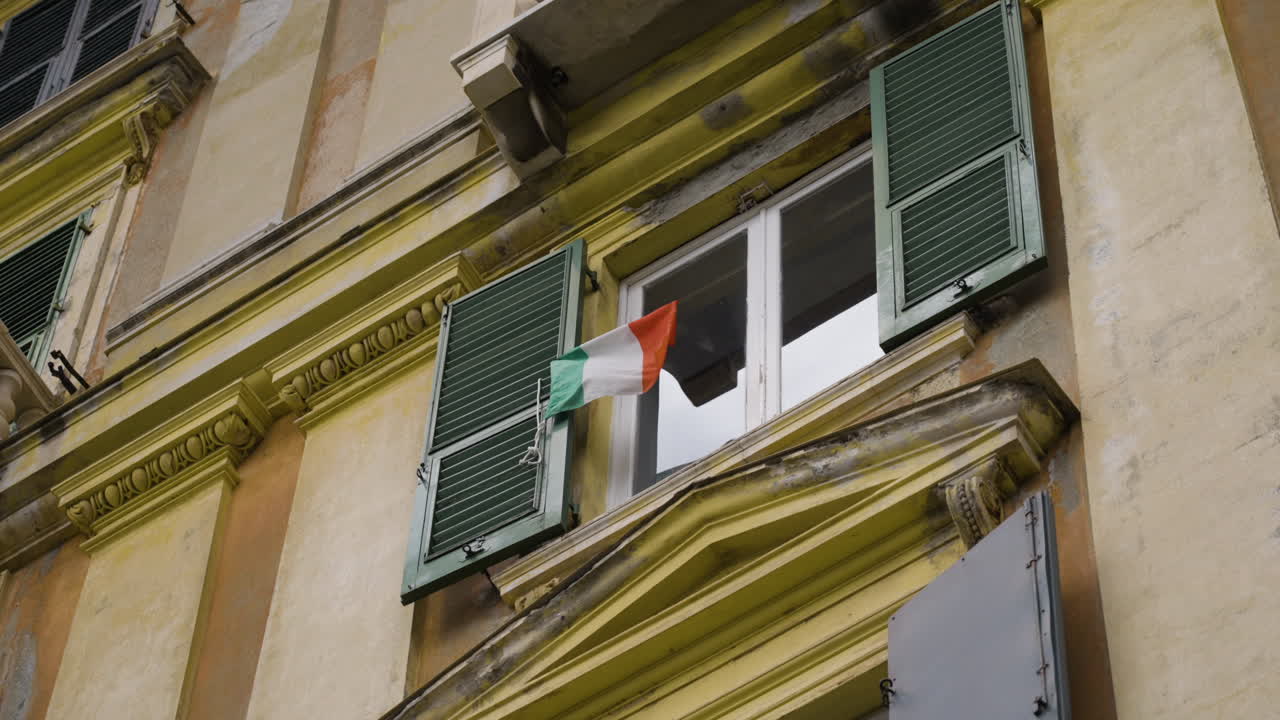 bandera italiana ondeando por el viento en el marco de una ventana en la fachada del edificio