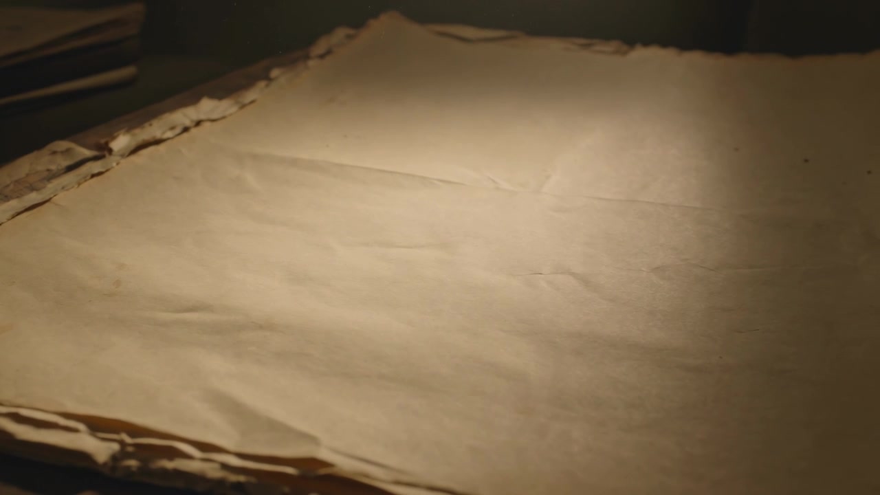 Panoramica della telecamera che rivela un singolo foglio invecchiato su un tavolo di legno, una lampada calda che illumina i bordi strappati di una pila.