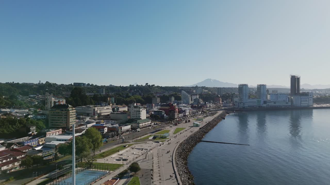 Drone capturing the coastal cityscape of Puerto Montt, showcasing the Diego Portales waterfront, buildings, and green hills, in Los Lagos Region, Chile. Pedestal Up