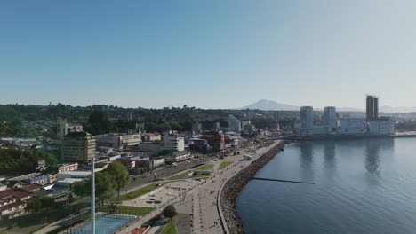 drone capturing the coastal cityscape of puerto montt, showcasing the diego portales waterfront, buildings, and green hills, in los lagos region, chile. pedestal up
