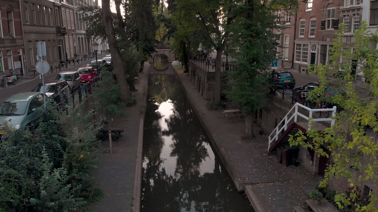 Vista aérea matinal recuada do canal Nieuwe Gracht na cidade holandesa medieval de Utrecht, ao nascer do sol, emergindo entre as árvores e revelando o nível superior da rua