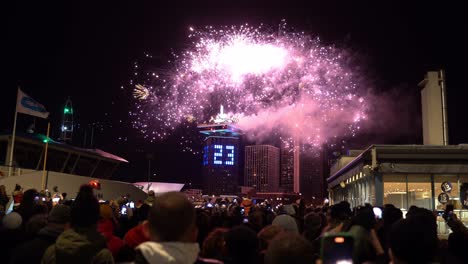 crowd of people observing firework and drone light show happening in an urban city at night