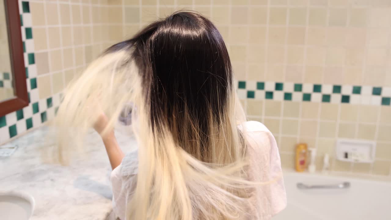 한 사람이 타일로 된 욕실에서 머리카락을 뒤집고 있습니다.