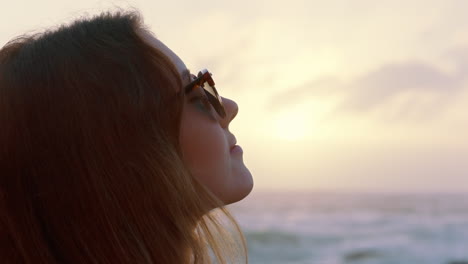 portrait of beautiful woman enjoying calm seaside at sunset exploring spirituality looking up praying contemplating journey relaxing on beach wearing sunglasses