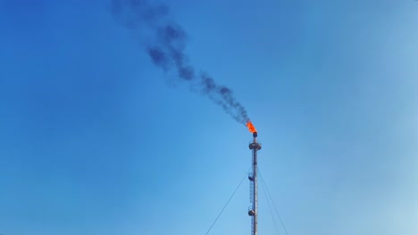 burning torch gas flare refinery against clear blue sky, minimal background