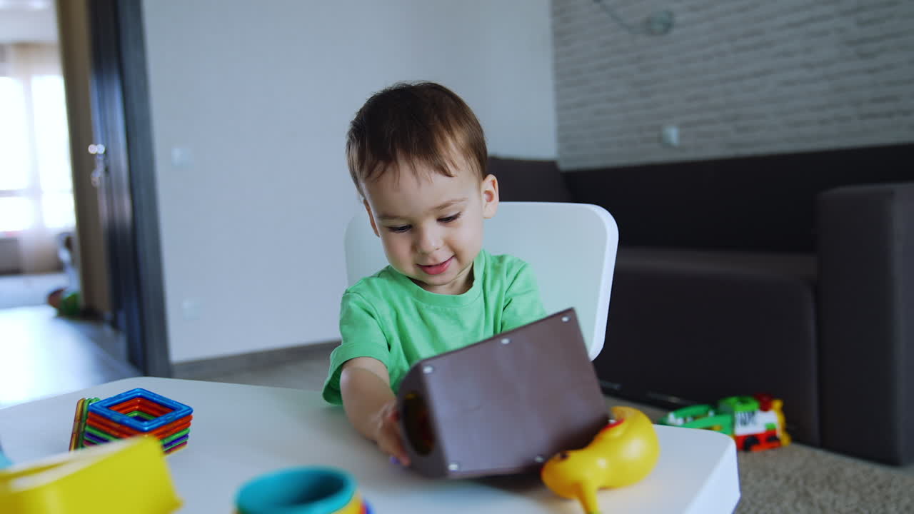 Sweet Caucasian boy plays with toys sitting at the desk. Lovely toddler in his playroom.