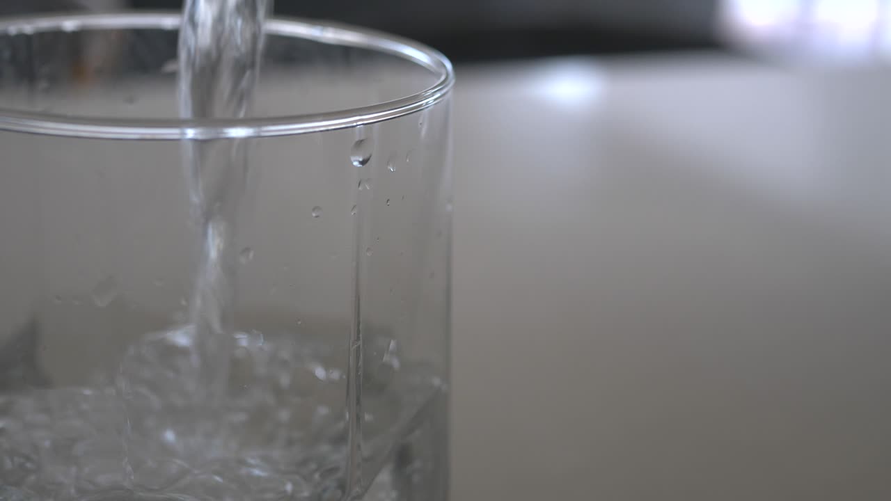 foto macro en cámara lenta de agua vertida en un vaso transparente con burbujas subiendo a la superficie