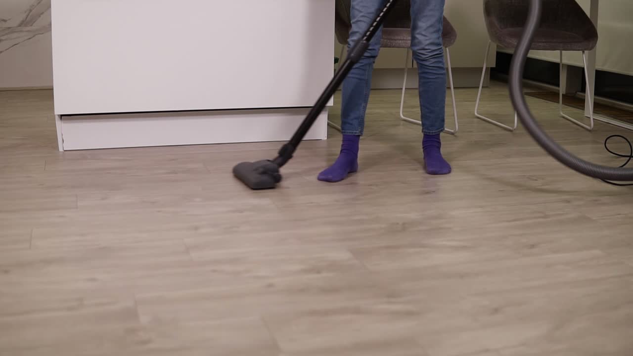 Cropped footage of a woman's legs vacuuming floor in kitchen, focused on cleaning in apartment. Housekeeping, lifestyle and creative people concept. Slow motion