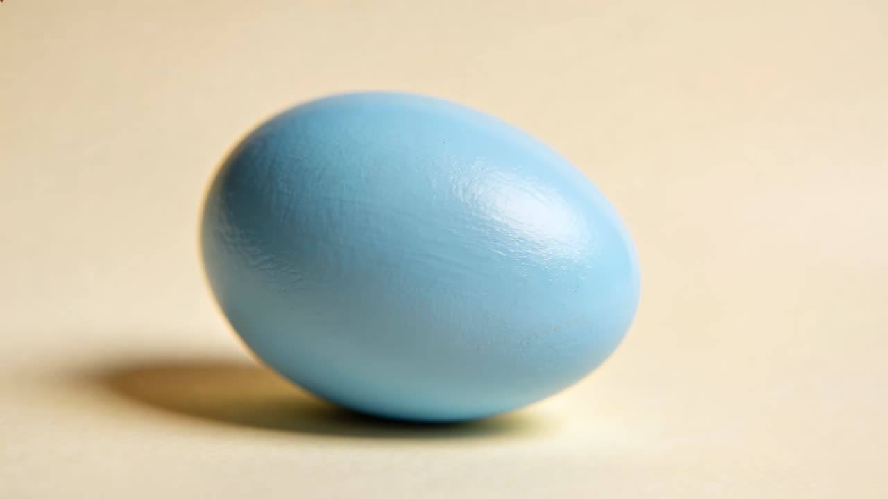 Rolling sky-blue egg moving on beige tabletop with soft shadow, tilt causing gravity settle upright