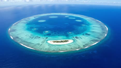 breathtaking aerial view of a circular atoll surrounded by vibrant blue waters, showcasing the intricate patterns of coral reefs and a serene island paradise