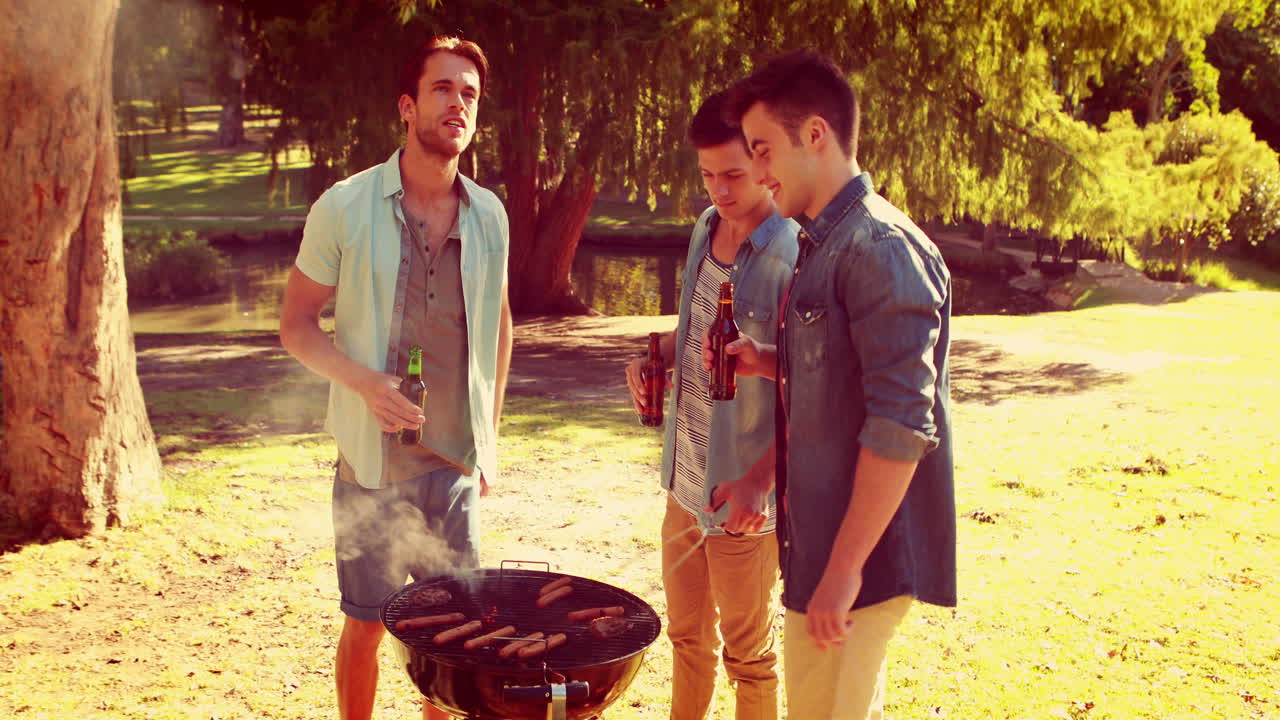Tre amici al parco che fanno un barbecue e bevono birra
