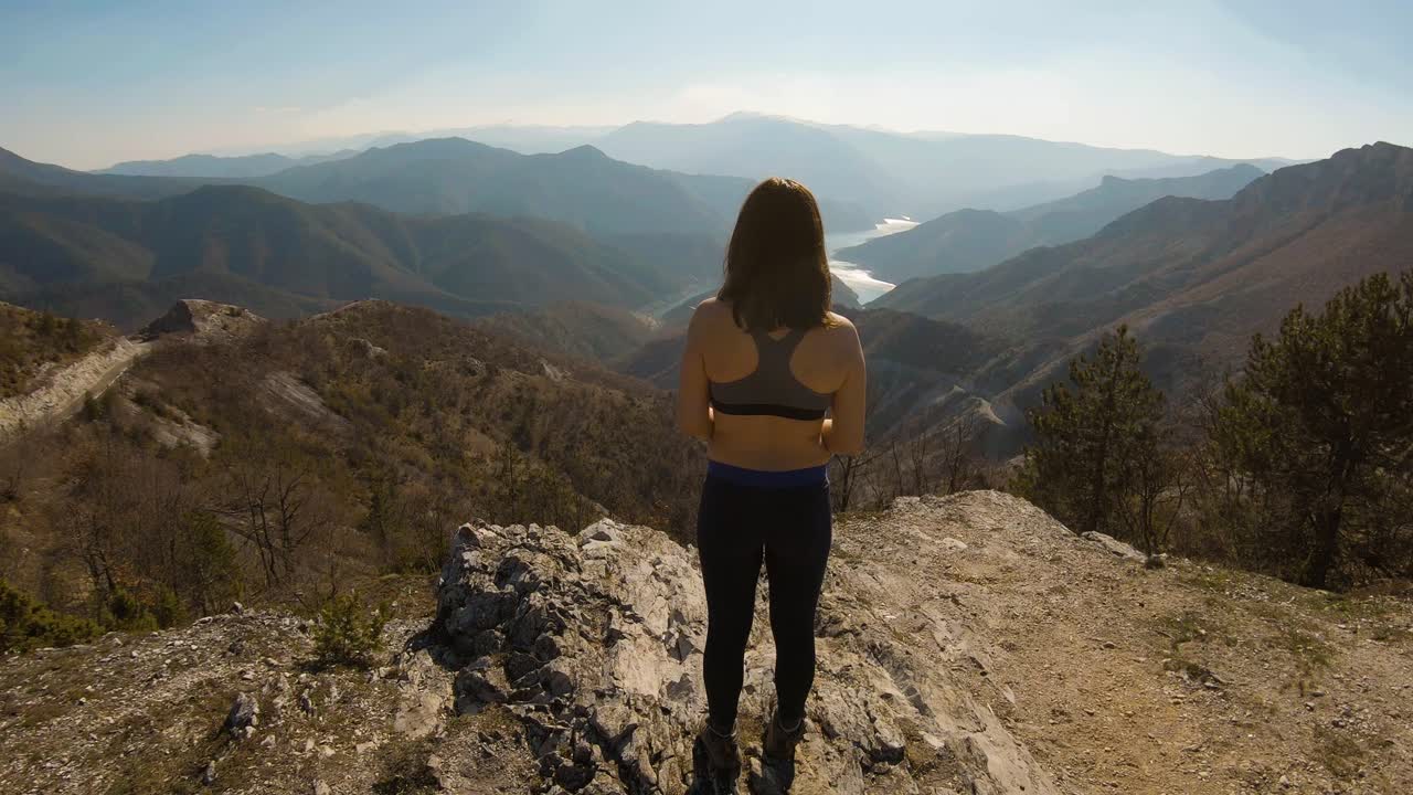 chica atleta parada en la cima de una montaña haciendo cola de caballo con un hermoso lago del cañón frente a ella