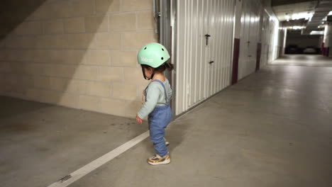 adorable toddler with green bike helmet walking in the garage - wide shot