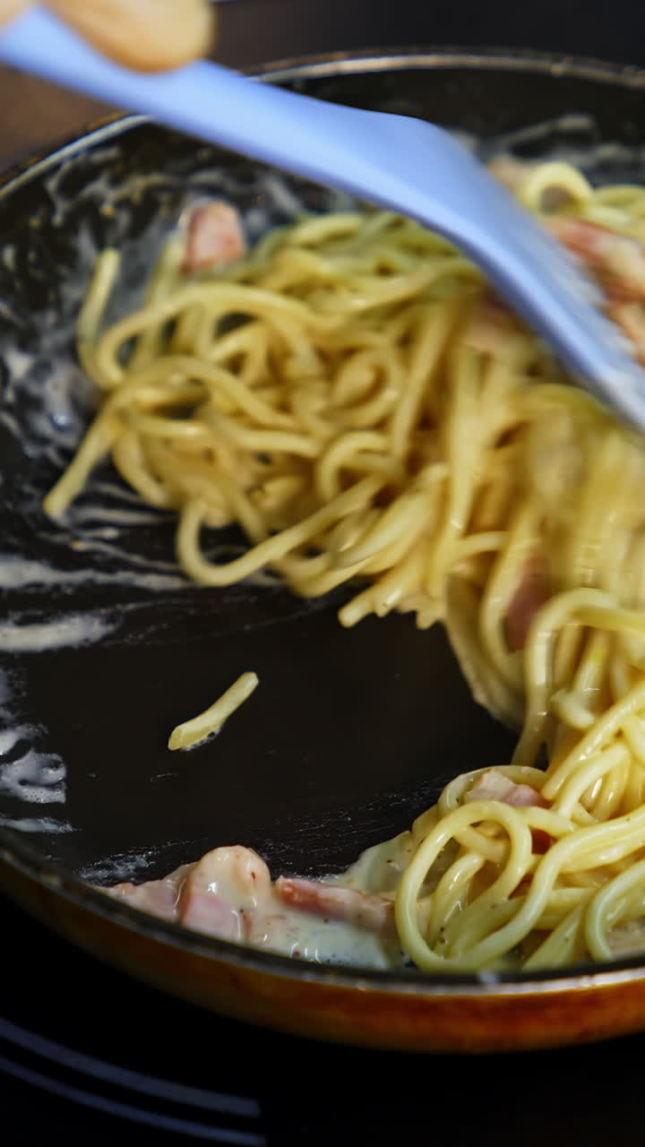 Frying pasta with bacon in tasty sauce. Cooking tasty dish in a frying pan. Chef cooks spaghetti pasta in a restaurant kitchen. Food ingredient. Cooking on cuisine. Cooked for gourmet. Vertical video