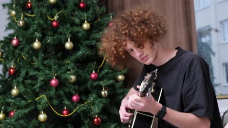 a curlyhaired guy plays the guitar on the background of a christmas tree christmas celebration a curlyhaired guy plays the guitar on the background of a christmas tree christmas celebration