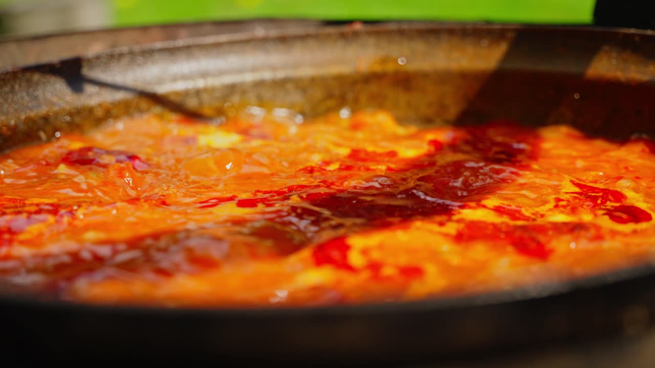 Cooking bubbling soup in black iron kettle outdoors over flames in rural forest setting, slow motion