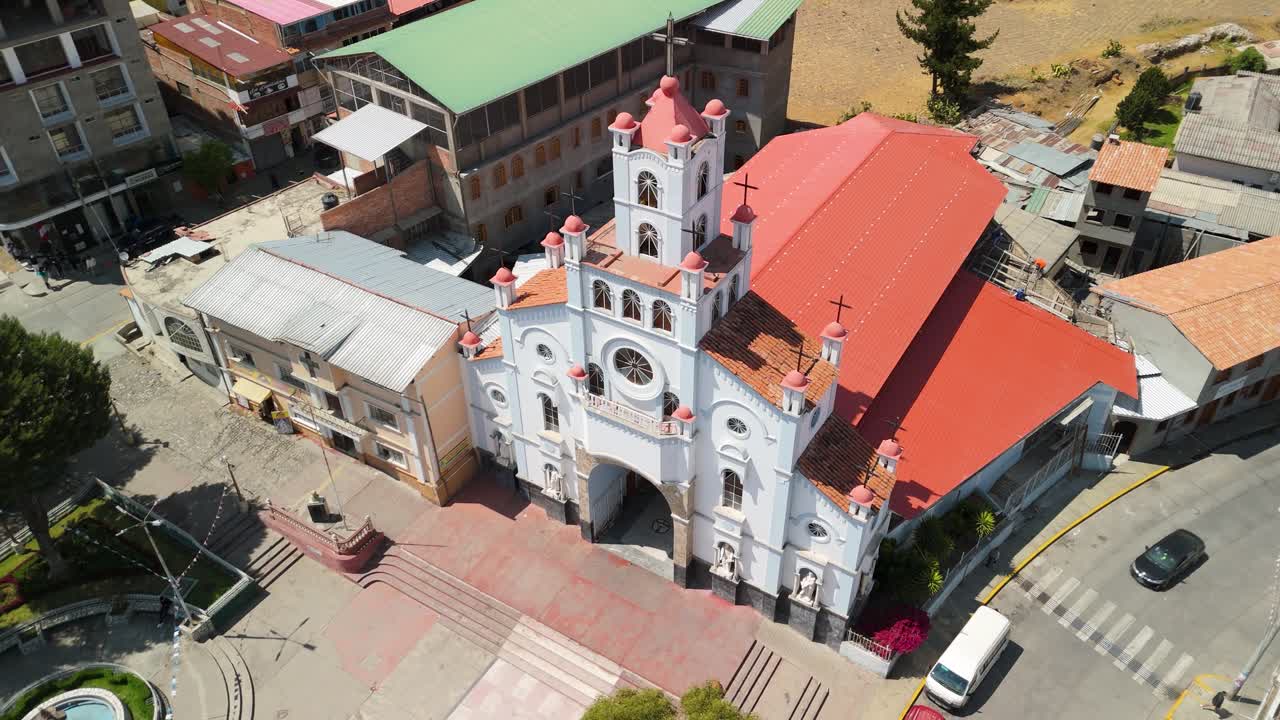 Aerial of historic Santuario de la Soledad church in Huaraz, Peru, drone shot rises tilting down for a beautiful view of the white facade, roof, surrounding streets and plaza