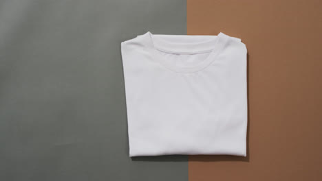 Video-of-flat-lay-of-folded-white-t-shirt-with-copy-space-on-grey-and-brown-background