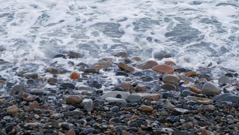 Einlaufende-Meereswellen-Spülen-über-Glatte,-Runde-Felsen-Am-Kiesstrand