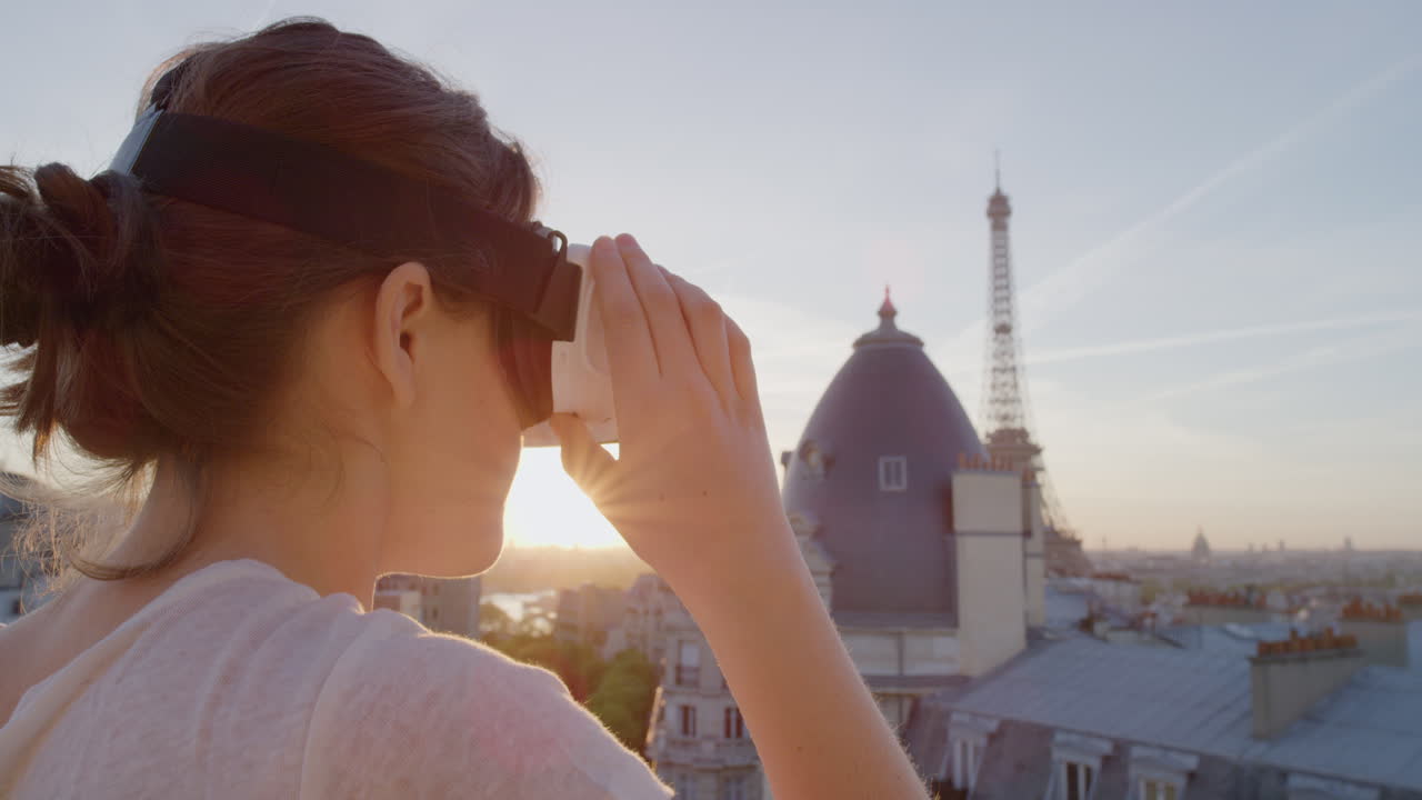 donna che usa un auricolare di realtà virtuale che si gode di esplorare l'esperienza del cyberspazio online sul balcone nella bellissima parigi al tramonto da vicino