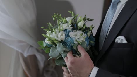 Groom-with-wedding-bouquet-in-his-hands-at-home.-White-shirt,-blue-tie,-jacket