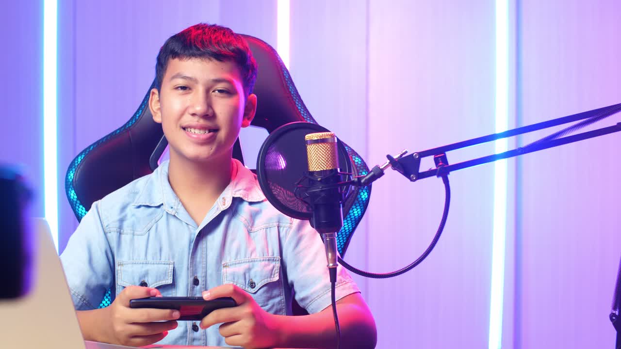 Excited Asian Kid Boy Playing Video Game With Mobile Phone Then Smiles To Camera While Live Stream