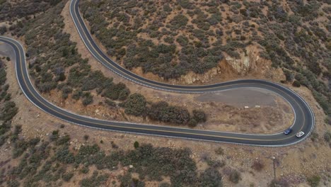 Orbiting-aerial-as-cars-take-sharp-switchback-turn-on-mountain-highway,-4K